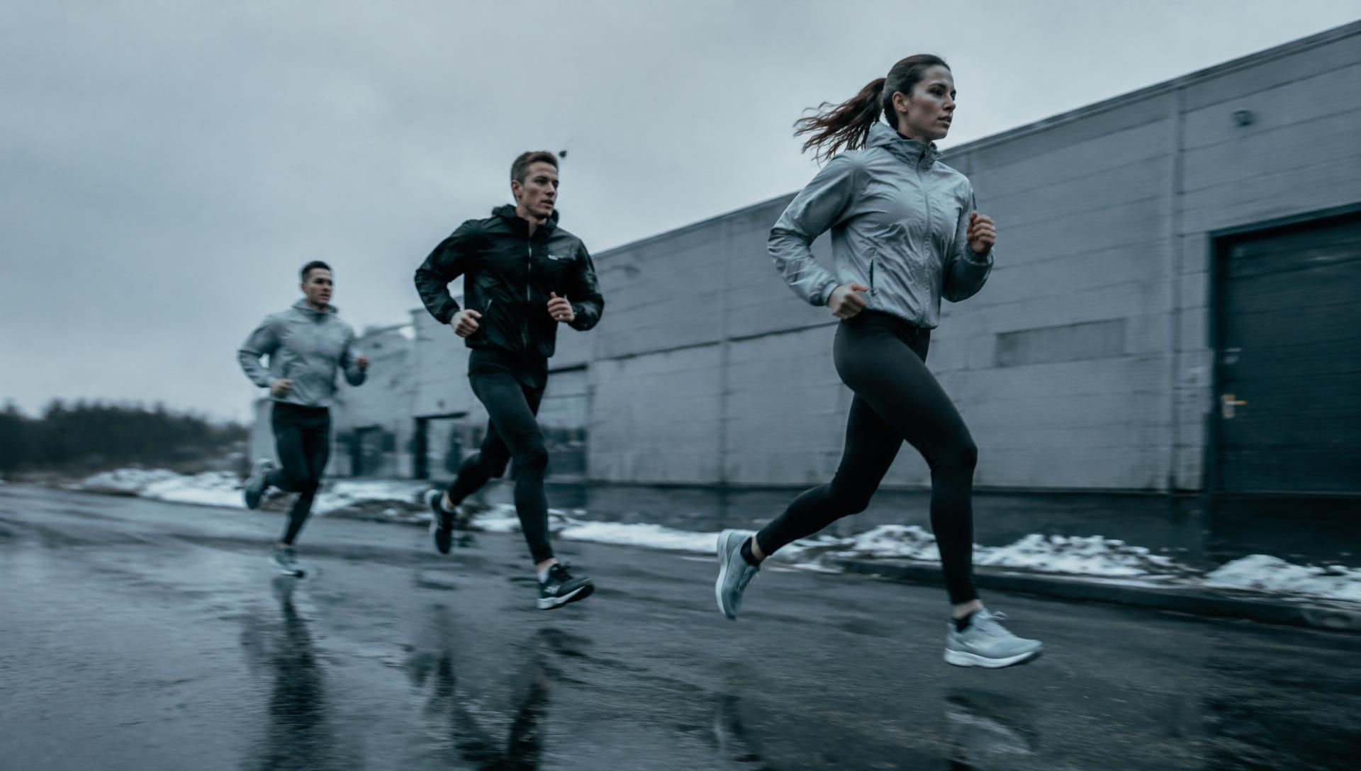 Athletes running outdoors past an industrial building